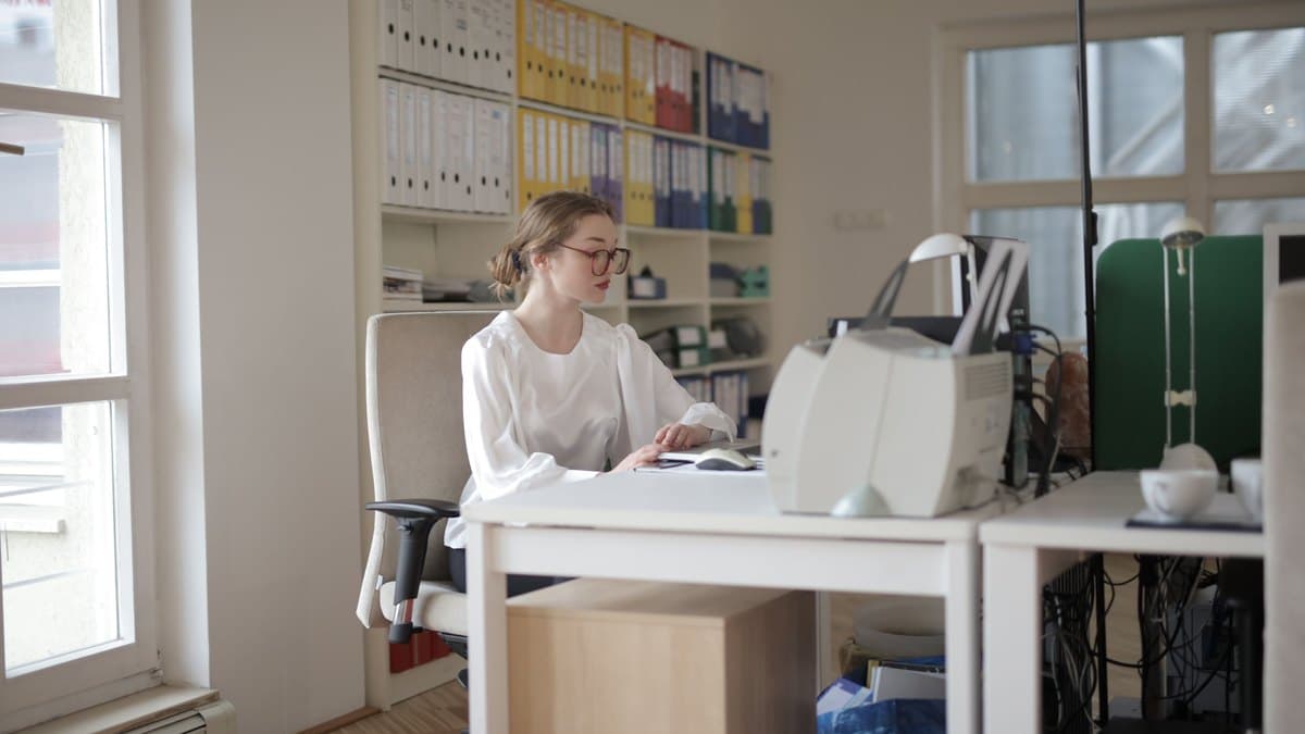 Junge Frau am Schreibtisch in einer Verwaltung, im Hintergrund bunte Aktenordner