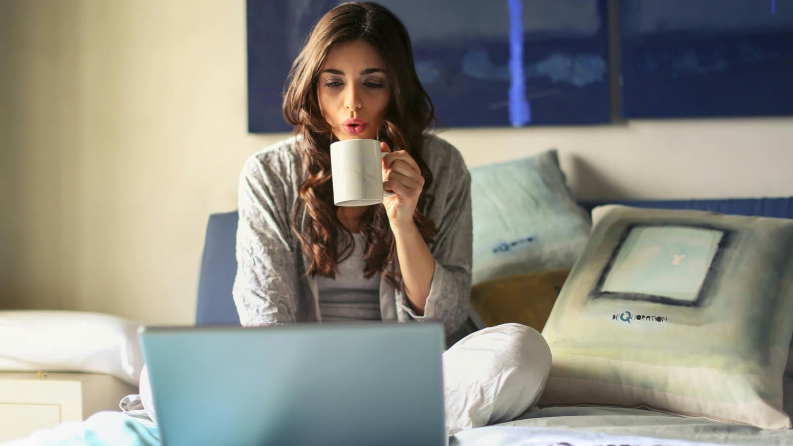 Frau lernt entspannt mit Kaffee am Laptop auf dem Sofa, Sinnbild für flexibles Online-Lernen statt Bibliothek