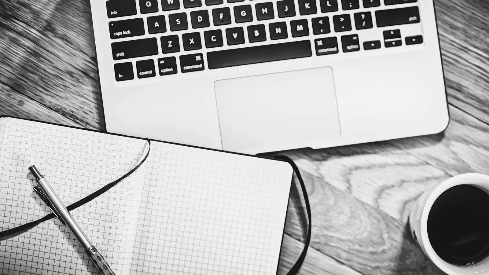 Laptop, Notizblock und Kaffee auf einem Schreibtisch, Sinnbild für das Schreiben einer juristischen Hausarbeit