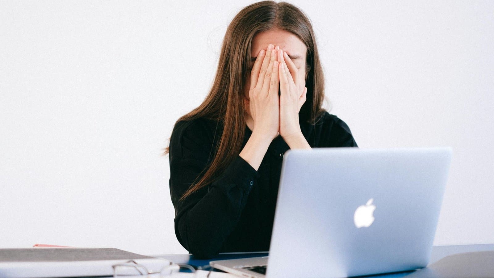 Erschöpfte Frau verbirgt das Gesicht in den Händen am Laptop, Sinnbild für Stress und psychische Belastung im Jurastudium