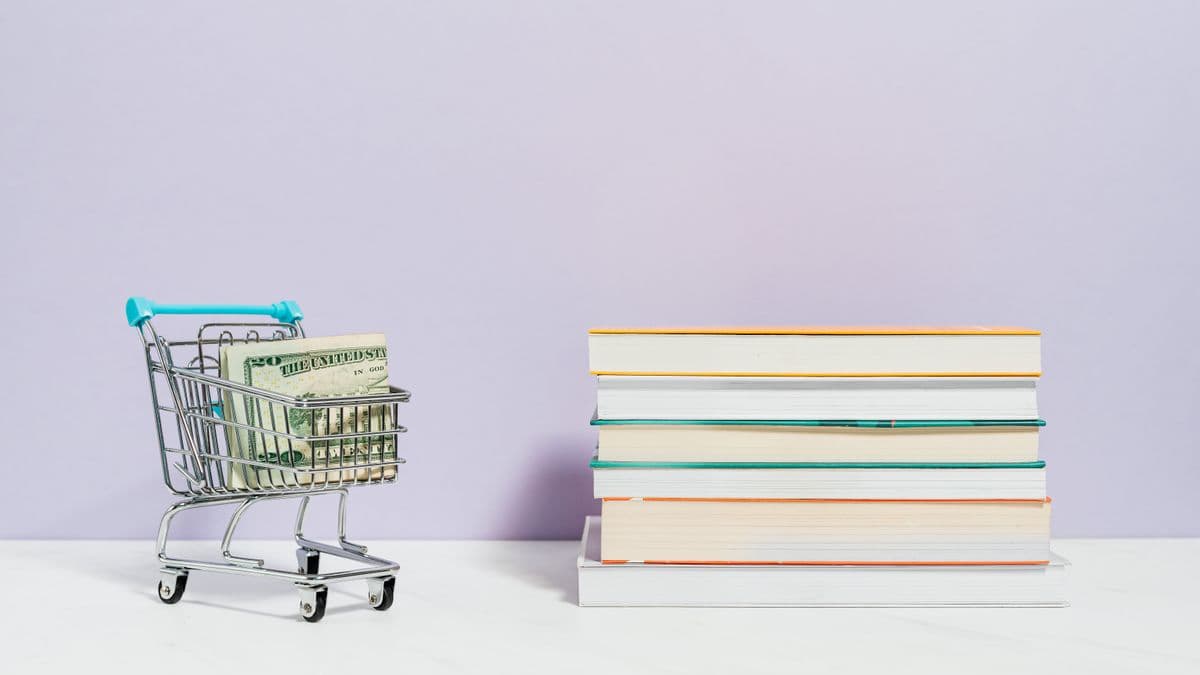 Bücherstapel neben einem Einkaufswagen mit Geldschein als Sinnbild für die Kosten eines Studiums.
