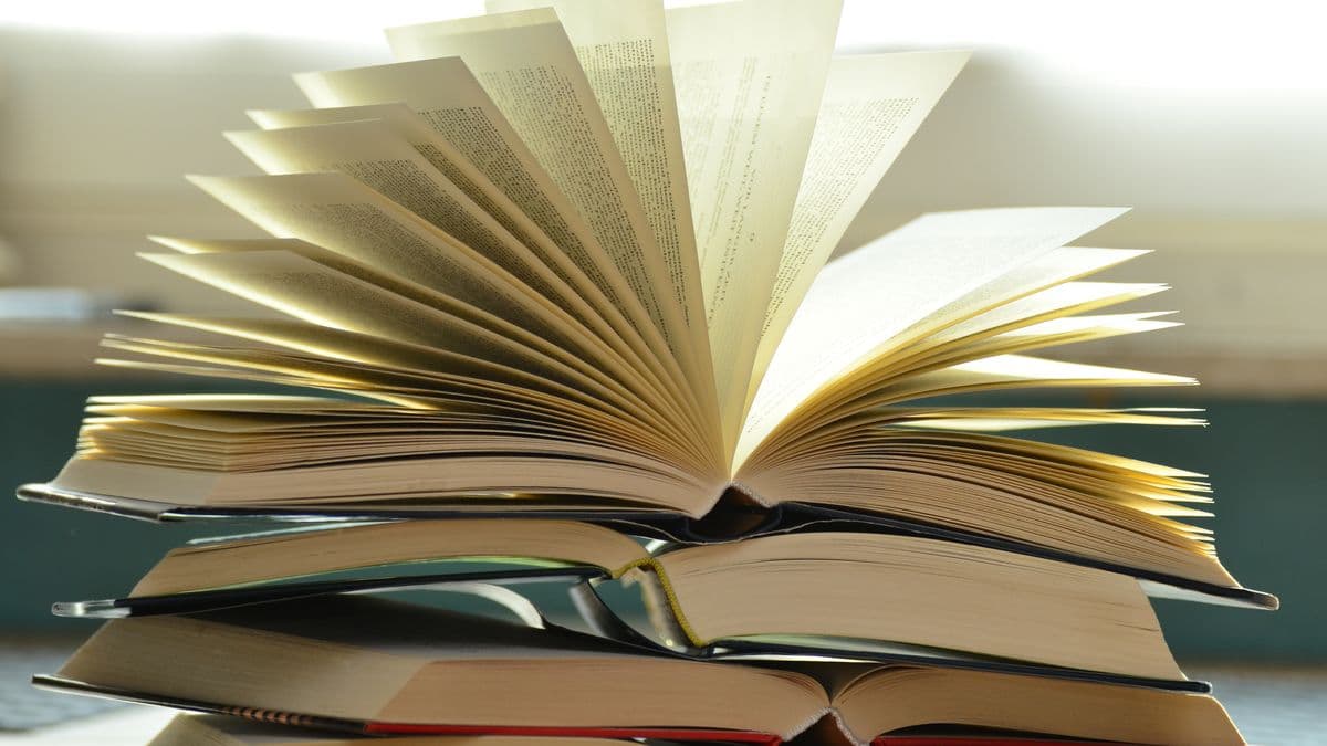 Aufgeschlagene Bücher stapeln sich im warmen Licht auf einem Schreibtisch.