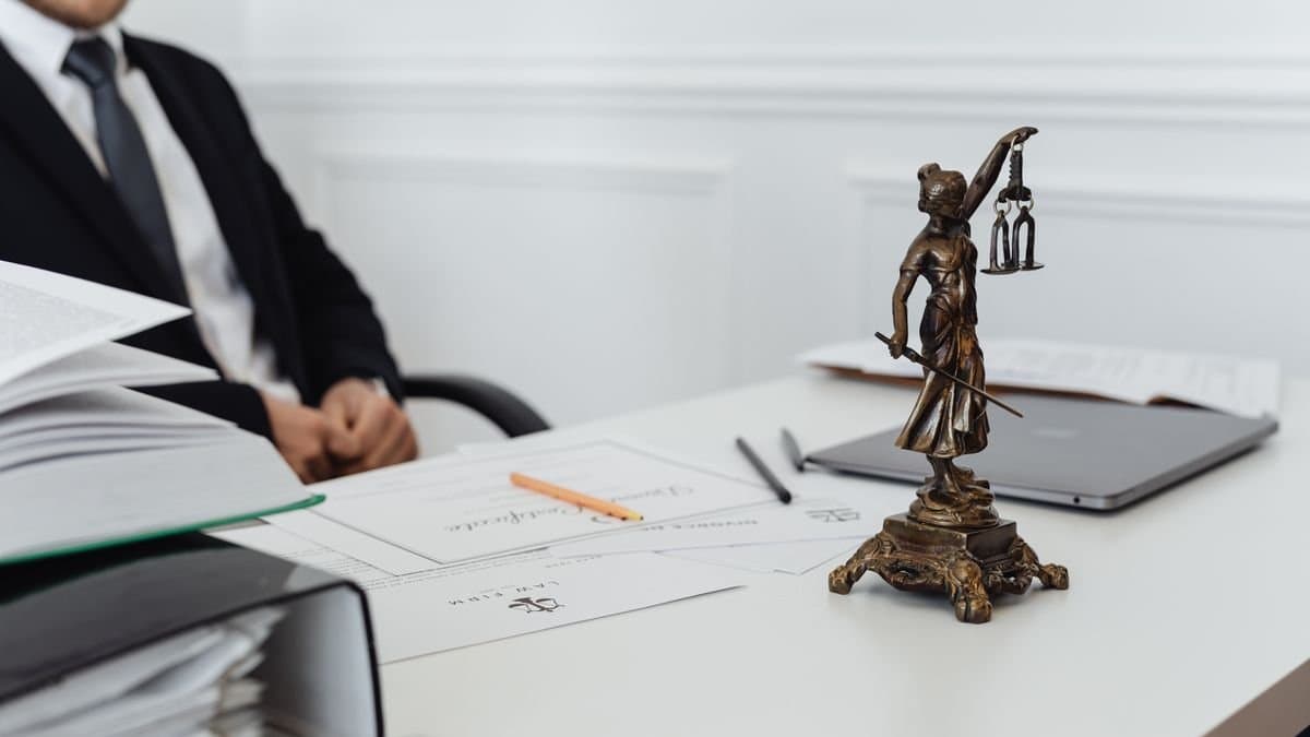 Anwalt am Schreibtisch mit Justitia-Statue, Akten und Dokumenten in einer Kanzlei