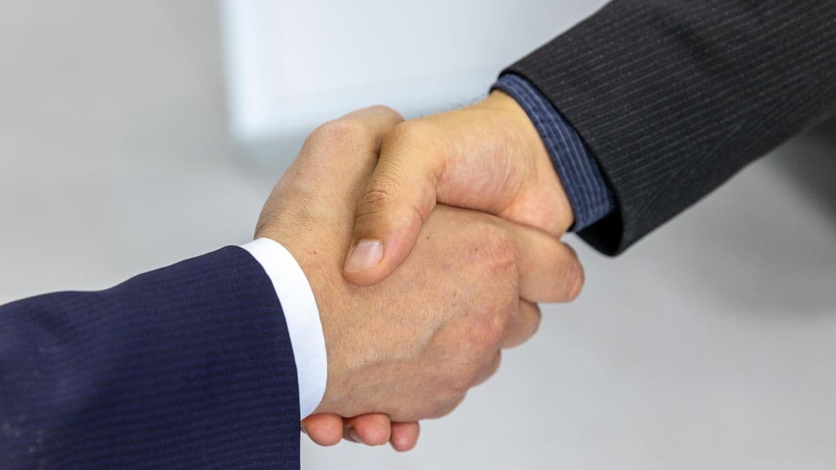 Zwei Personen in Anzügen geben sich per Handschlag die Hand, Sinnbild für den geschäftlichen Kontakt vor dem Vertrag.