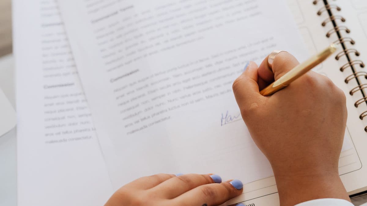 Eine Person unterschreibt mit einem Stift ein mehrseitiges Dokument auf einem Schreibtisch