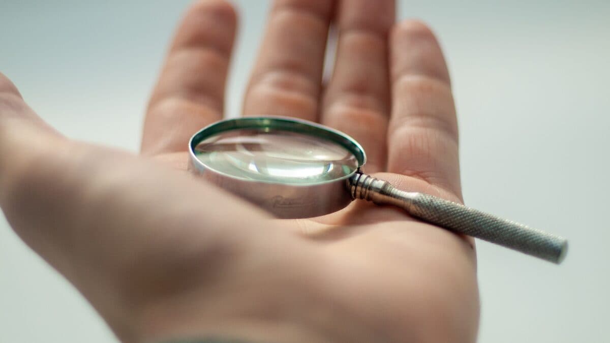 Eine offene Hand hält eine kleine Lupe vor hellem Hintergrund