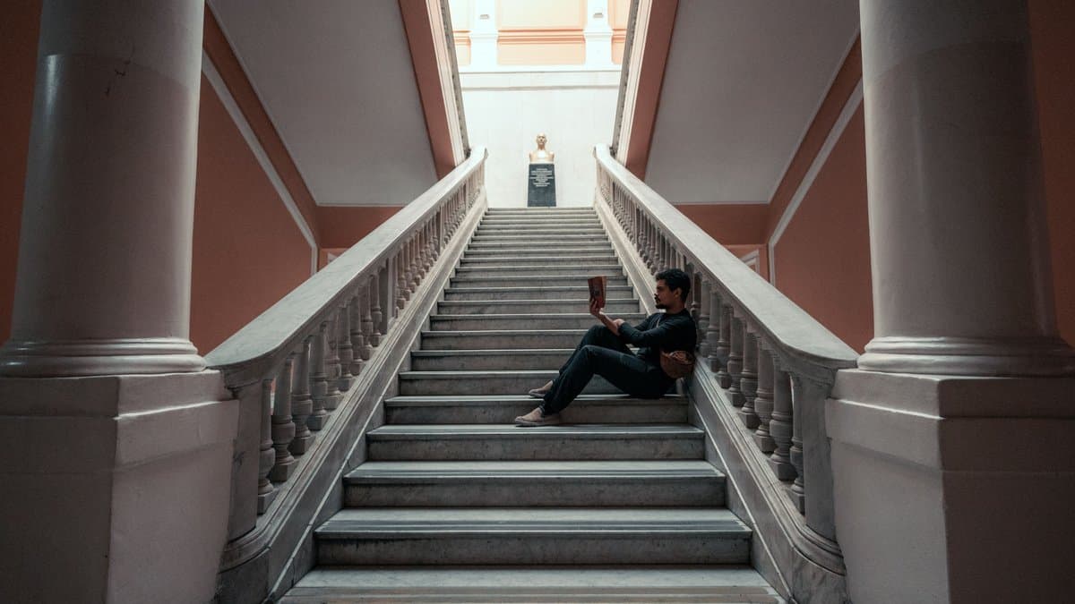 Student sitzt mit einem Buch auf der Marmortreppe eines Universitätsgebäudes und liest