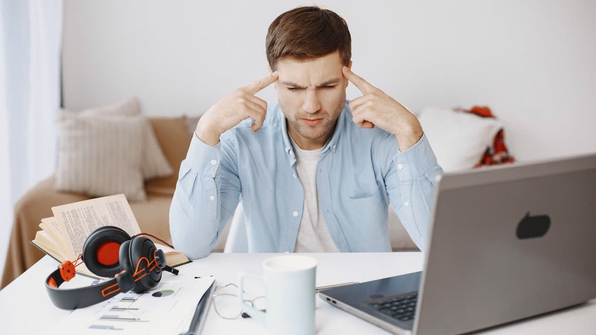 Person lernt am Schreibtisch mit Laptop, Unterlagen und Kopfhörern.