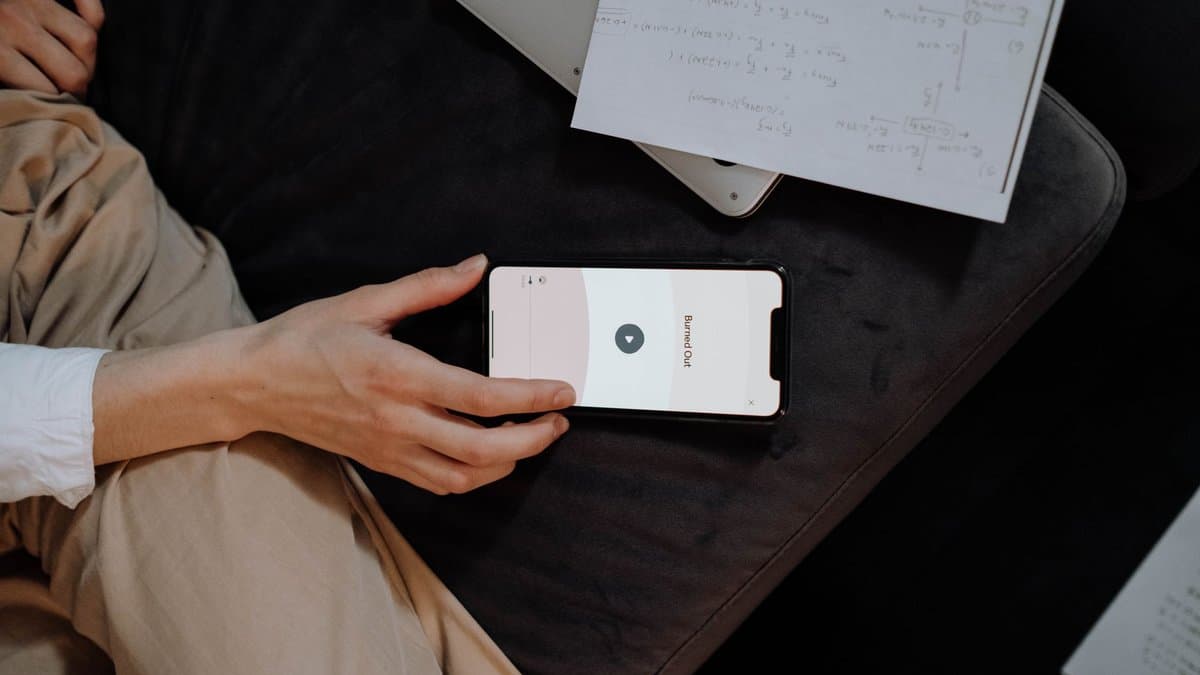 Hand hält ein Smartphone mit Lern-App, daneben Notizen und ein Laptop auf dem Schreibtisch