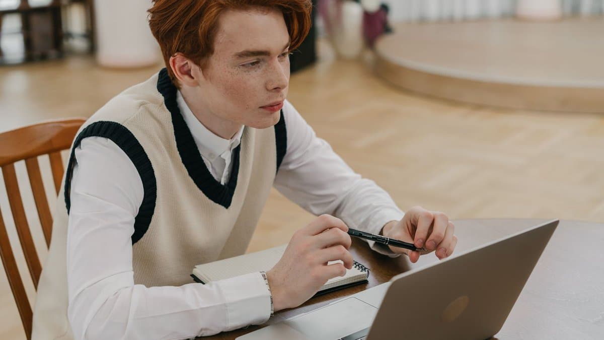 Junger Mann lernt konzentriert zu Hause am Laptop mit Notizbuch