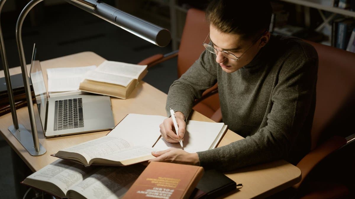 Junger Student macht sich am Schreibtisch Notizen aus einem aufgeschlagenen Buch