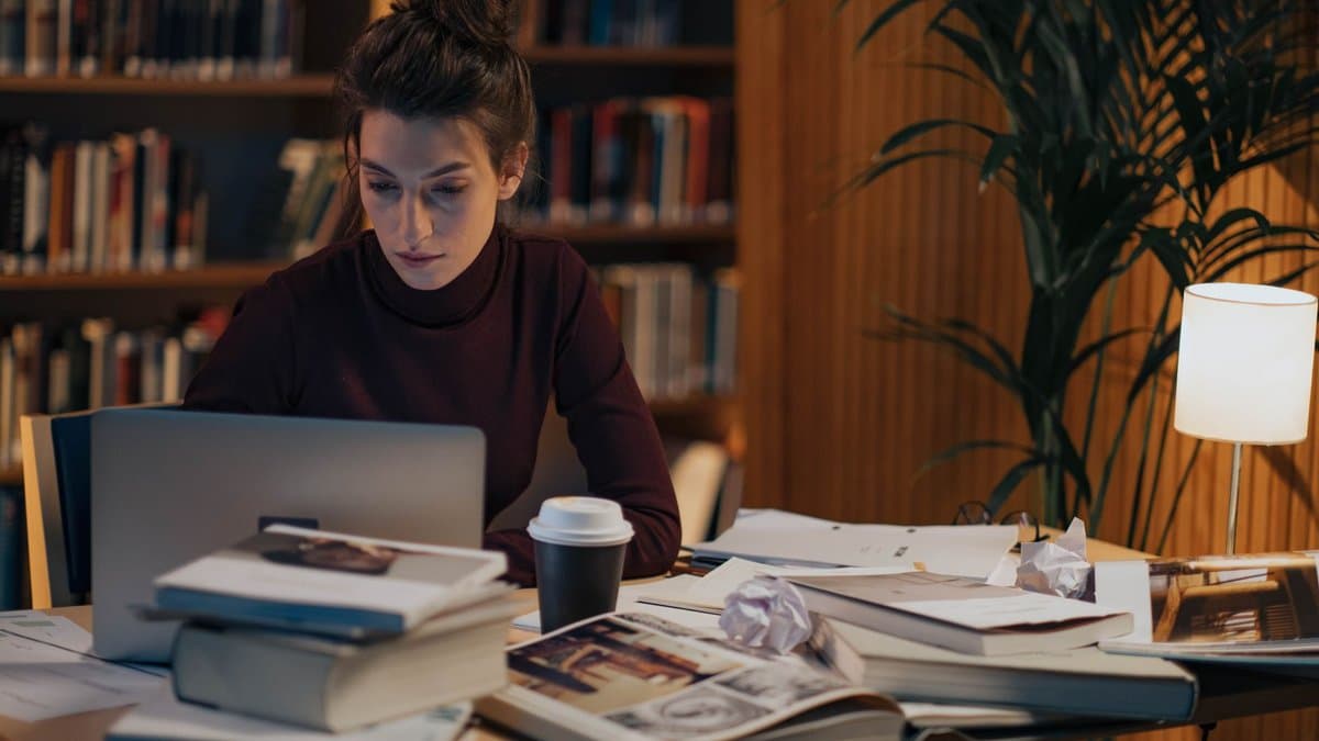 Studentin arbeitet konzentriert an einem Schreibtisch mit Büchern und Laptop in einer Bibliothek.
