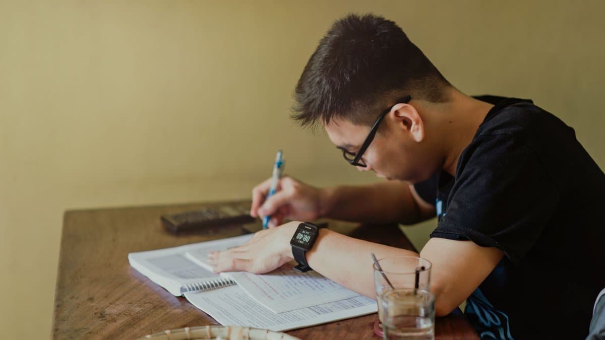 Ein Student sitzt konzentriert am Schreibtisch und macht sich Notizen zu einem aufgeschlagenen Buch