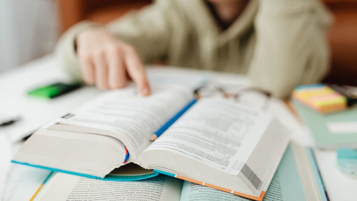 Person arbeitet konzentriert mit aufgeschlagenen Büchern und Notizen am Schreibtisch.