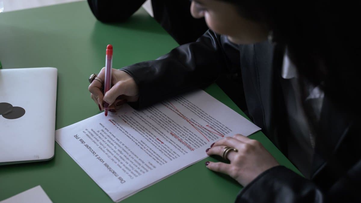 Person in Businesskleidung markiert mit rotem Stift Korrekturen auf einem ausgedruckten Text am Schreibtisch