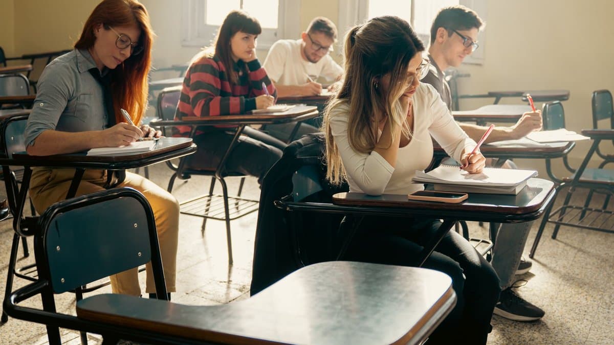 Studierende schreiben konzentriert an Klapptischen in einem Seminarraum mit hohen Fenstern