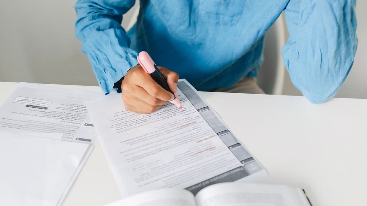Person markiert mit einem Textmarker Stellen in einem Dokument, daneben liegt ein aufgeschlagenes Buch