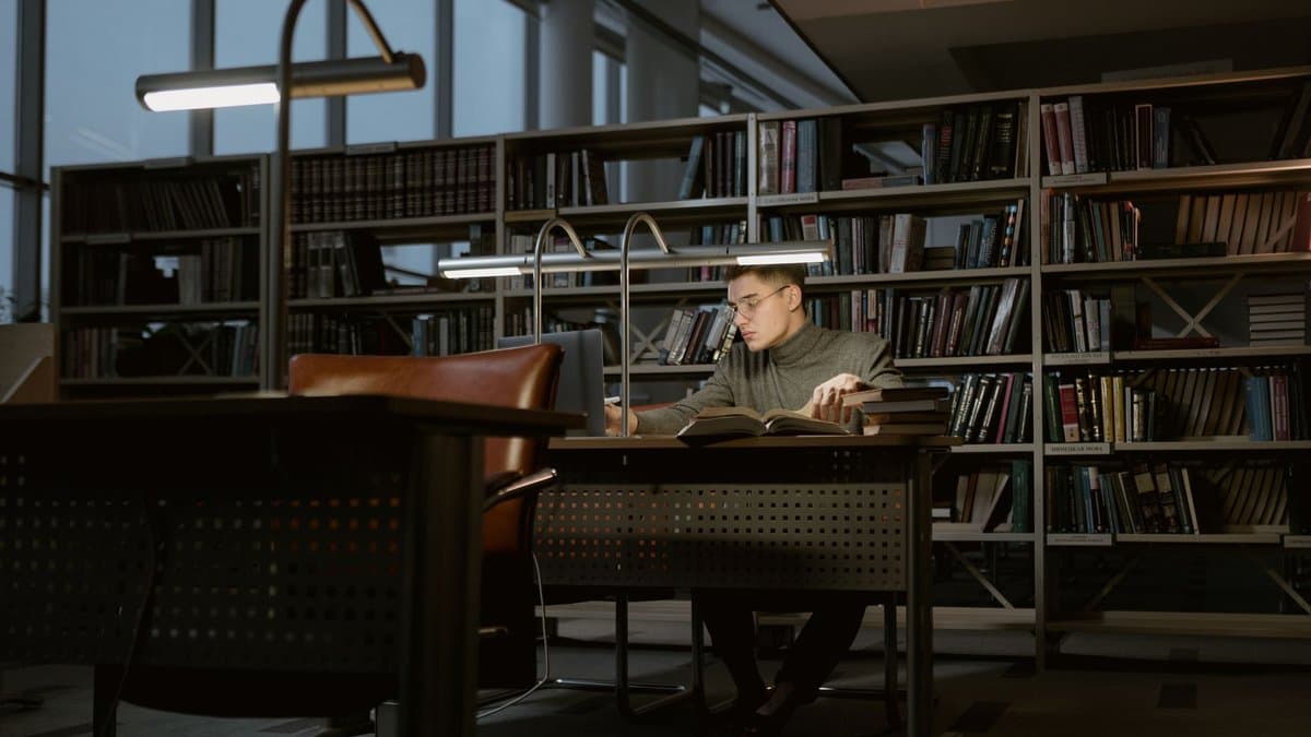 Ein Student arbeitet allein an einem Einzeltisch in einer Bibliothek, umgeben von hohen Bücherregalen