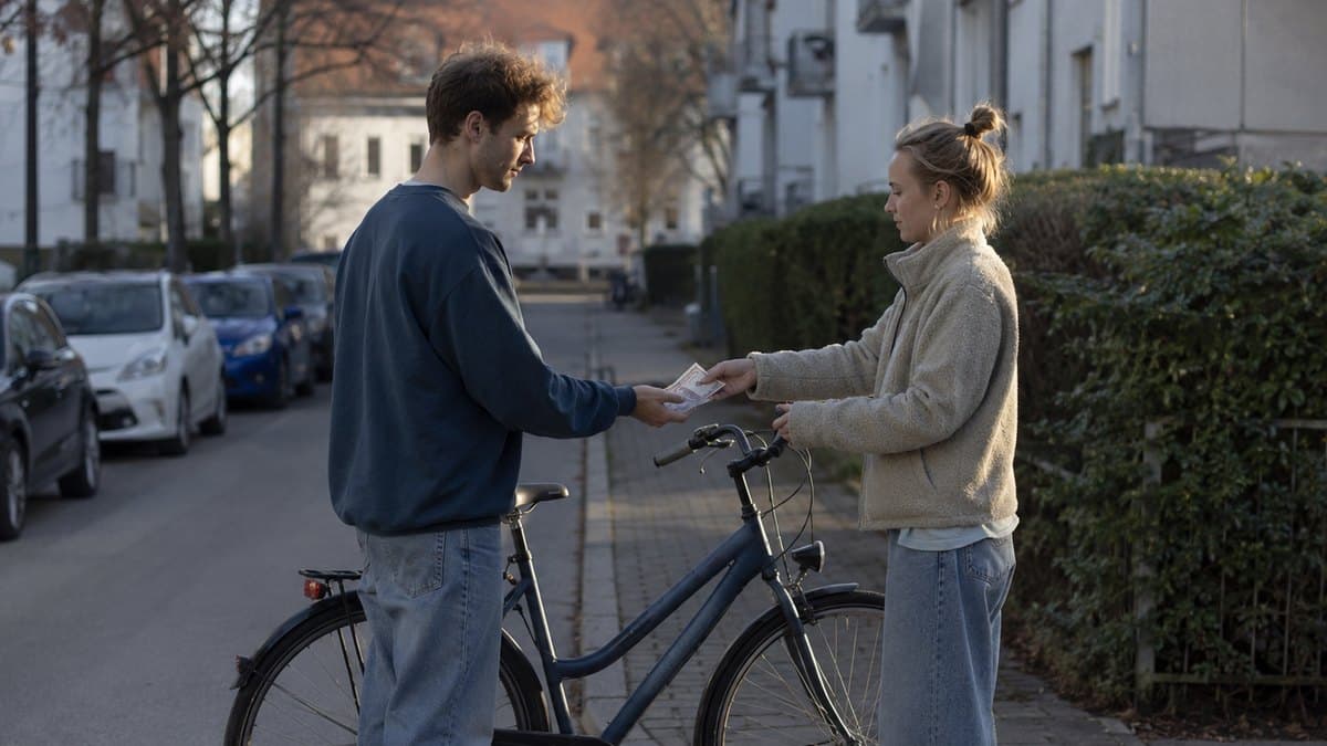 Junger Mann reicht einer Frau auf einer Wohnstraße Geldscheine, während sie ein gebrauchtes Fahrrad am Lenker hält