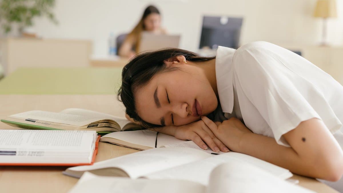 Studentin schläft am Schreibtisch zwischen aufgeschlagenen Büchern in einer Bibliothek