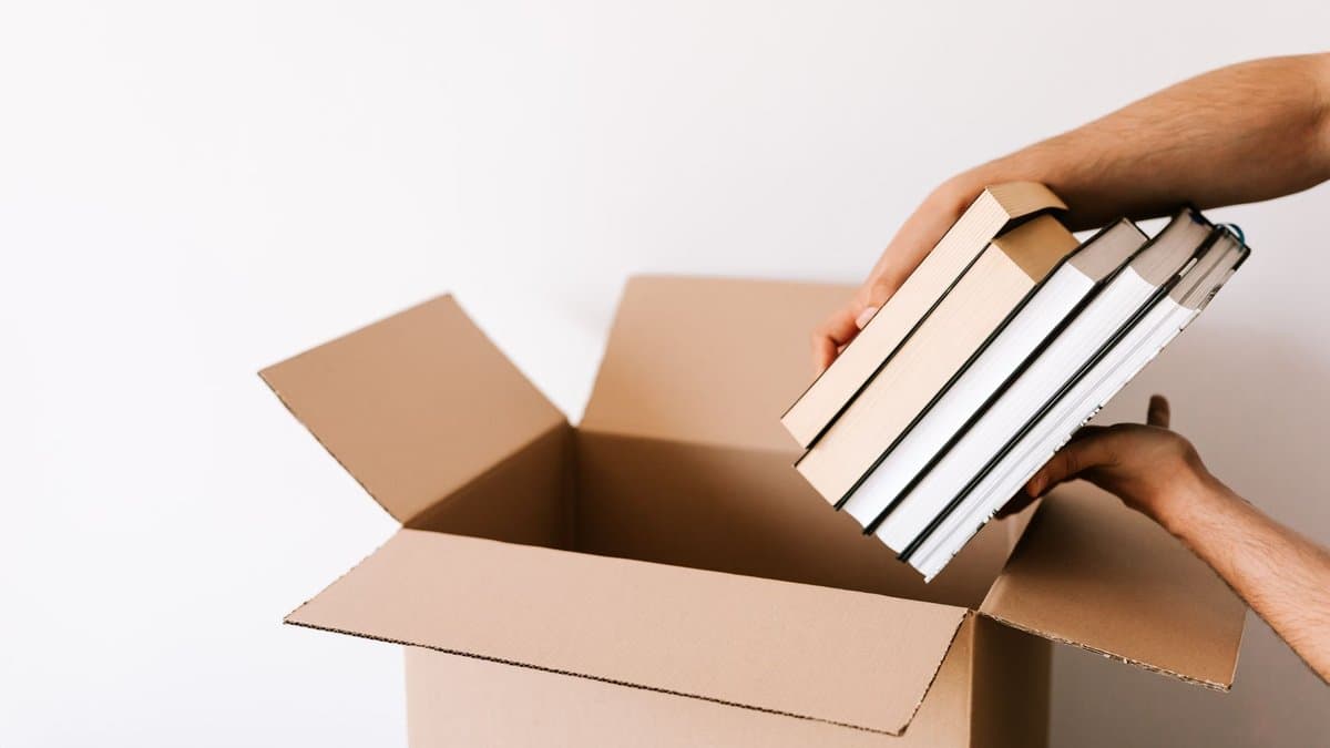 Hände legen einen Stapel Bücher in einen offenen Umzugskarton
