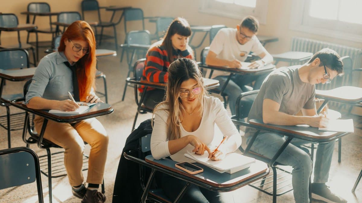 Studierende schreiben an einzelnen Tischen in einem hellen Raum konzentriert eine Klausur