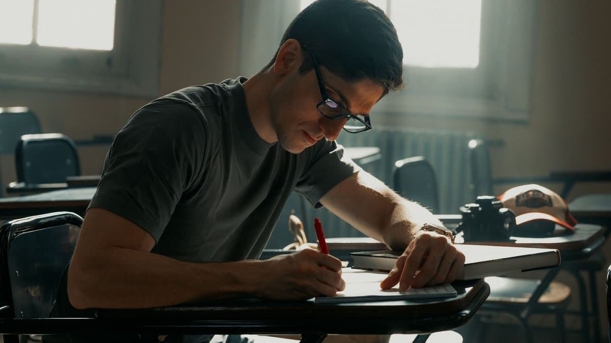 Student sitzt konzentriert schreibend an einem Tisch im hellen Seminarraum
