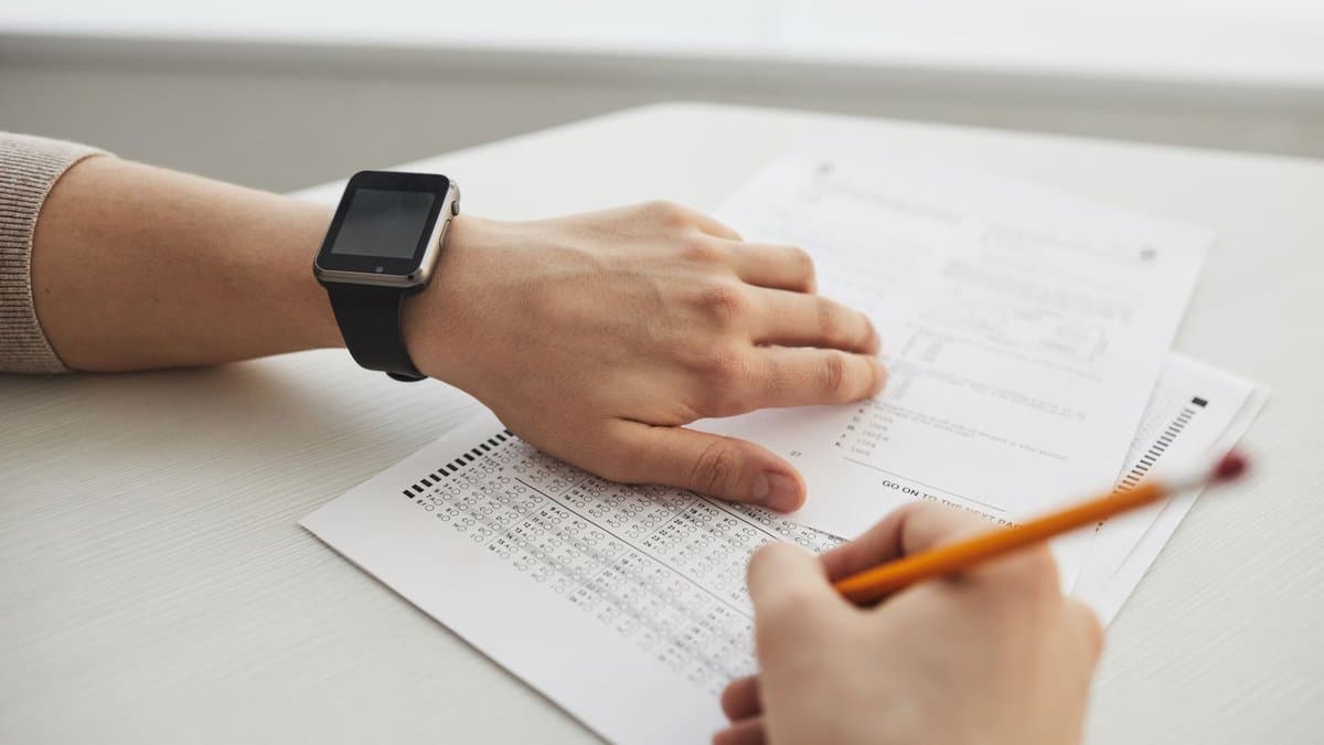 Hände über einem Antwortbogen mit Ankreuzraster, eine Hand hält einen Bleistift über den Antwortfeldern