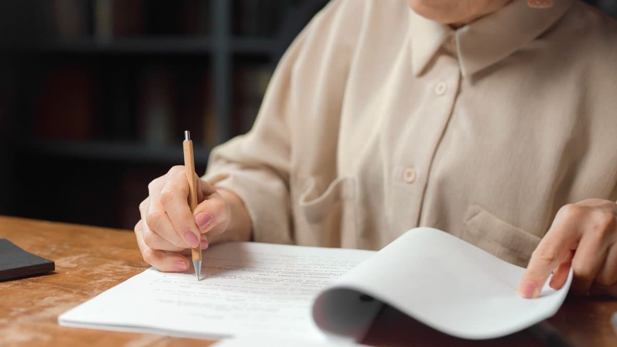 Frau geht am Schreibtisch mit dem Stift in der Hand einen handgeschriebenen Text durch