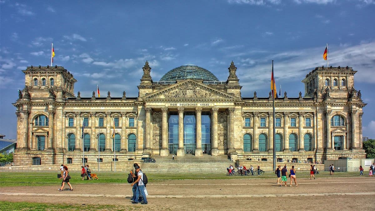 Menschen auf der Wiese vor dem Reichstagsgebäude in Berlin mit Glaskuppel und wehenden Fahnen