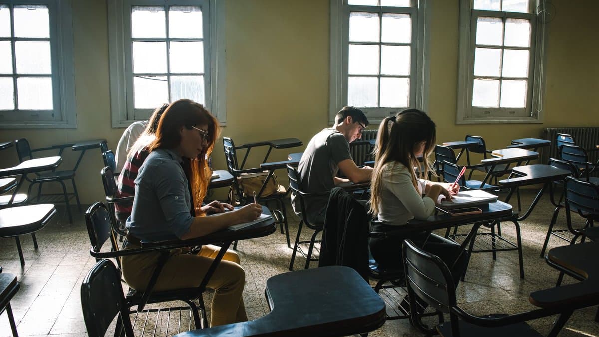 Studierende schreiben an Einzeltischen in einem hellen Prüfungssaal