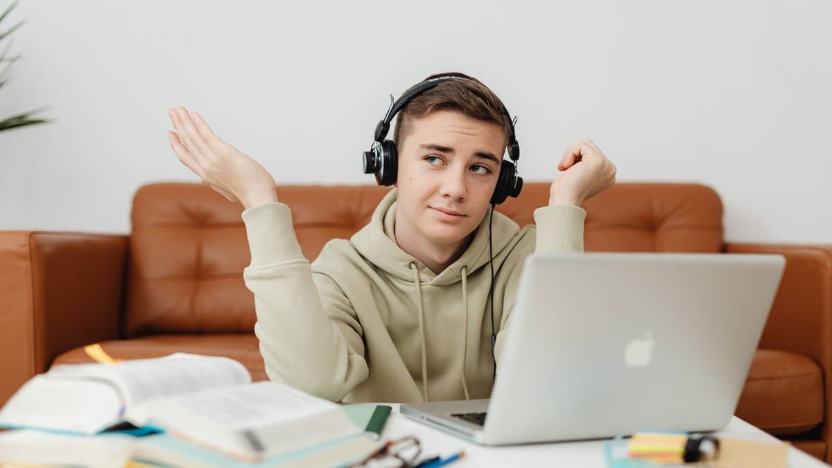 Student mit Kopfhörern vor dem Laptop, daneben aufgeschlagene Bücher und Notizblöcke