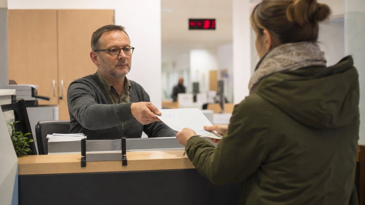 Ein Sachbearbeiter reicht einer Bürgerin am Schalter eines Bürgeramts ein gestempeltes Dokument über den Tresen.