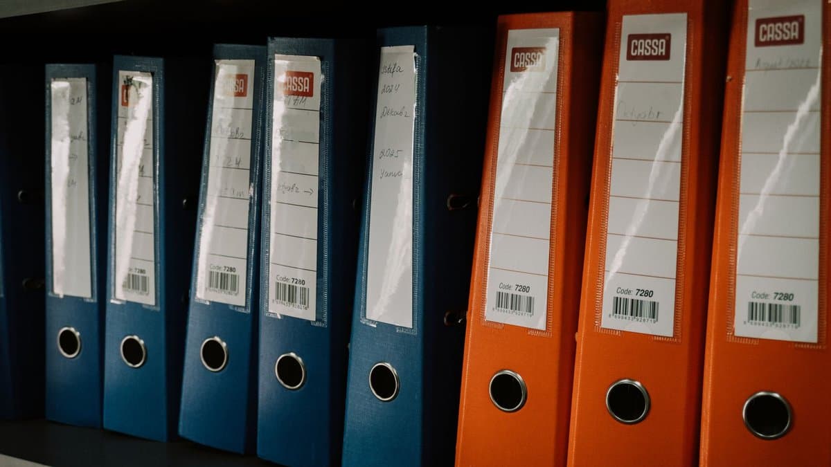 Reihe blauer und oranger Aktenordner mit handbeschrifteten Rückenschildern in einem Regal