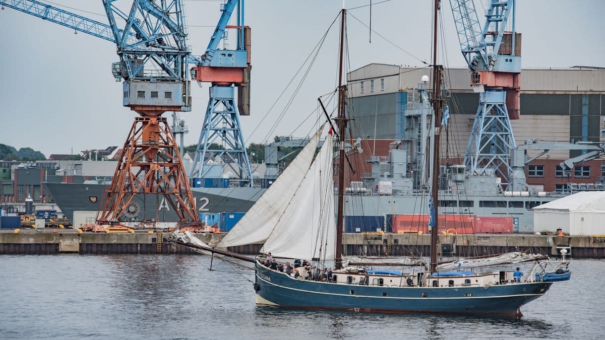 Klassisches Segelschiff fährt durch den Kieler Hafen, im Hintergrund die Werftkräne