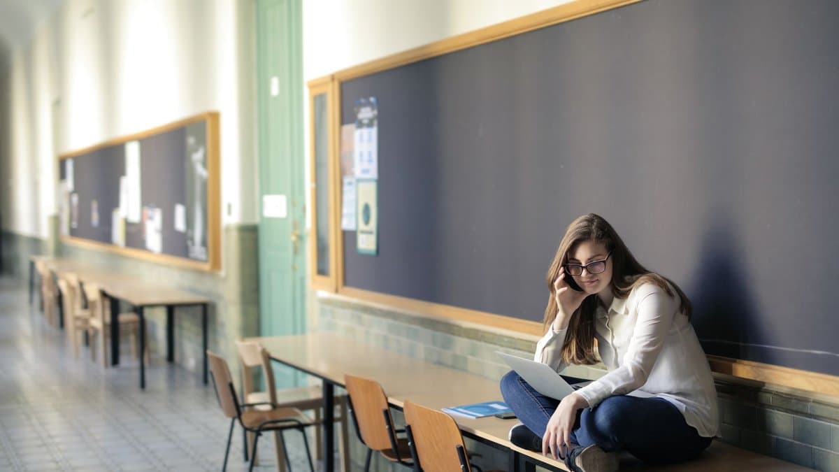 Studentin sitzt mit Laptop auf einem Tisch im Flur eines Universitätsgebäudes und lernt