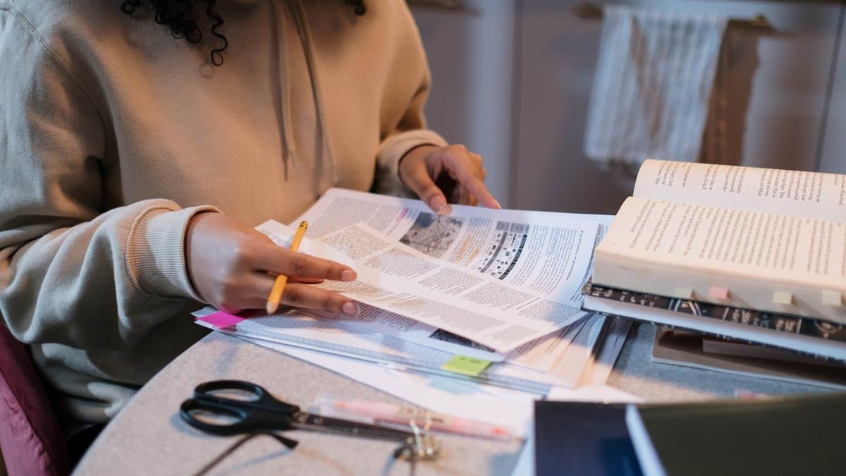 Studentin sitzt mit Bleistift vor mehreren aufgeschlagenen Büchern und Papieren und liest eine Textseite