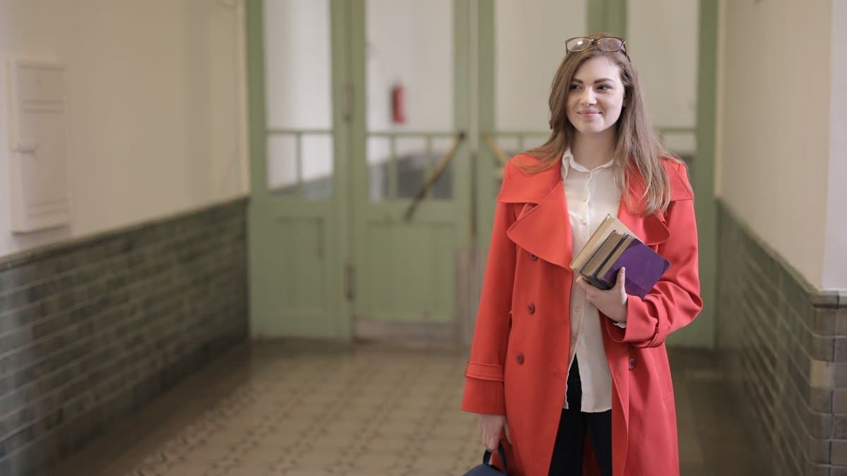 Studentin mit Büchern und Tasche steht im Flur eines Universitätsgebäudes