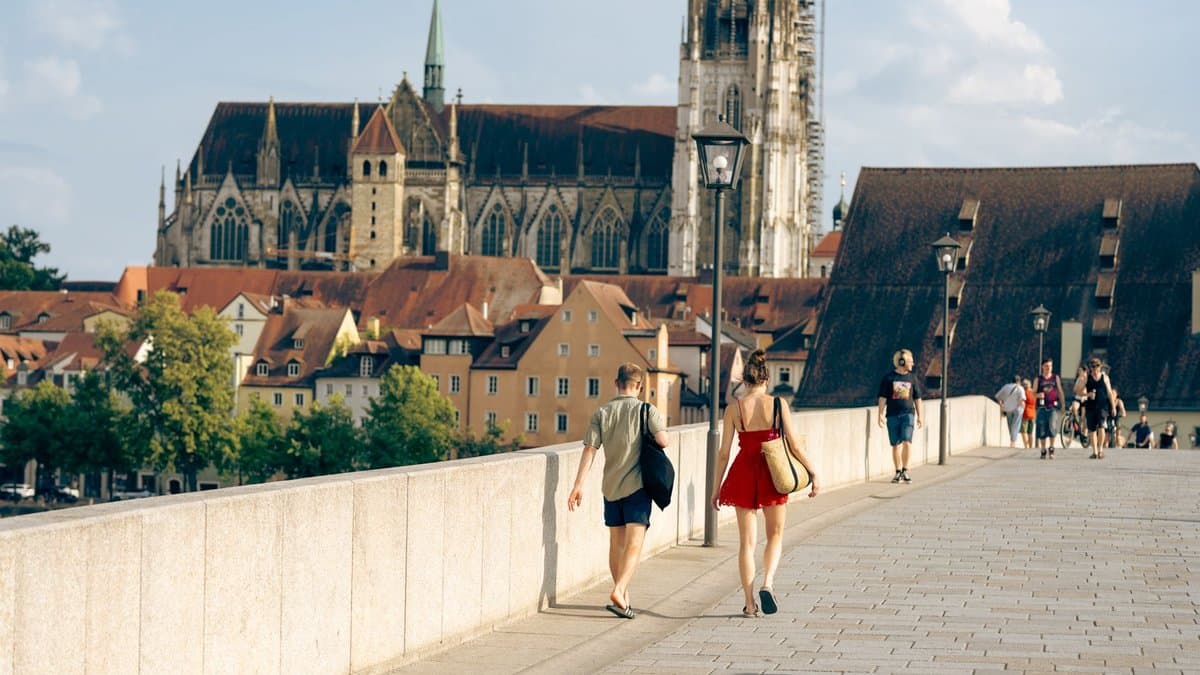 Zwei Studentinnen gehen über die Steinerne Brücke in Regensburg, im Hintergrund der Dom St. Peter