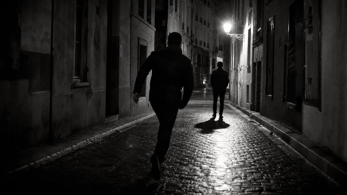 Nächtliche Gasse, eine dunkle Gestalt geht auf eine zweite zu, die mit dem Rücken zu ihr steht