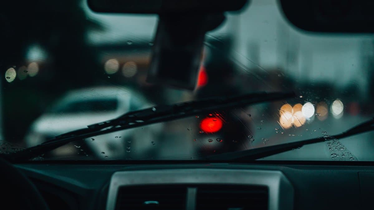 Blick aus einem parkenden Auto durch eine regennasse Windschutzscheibe auf eine nächtliche Straße mit Ampellichtern