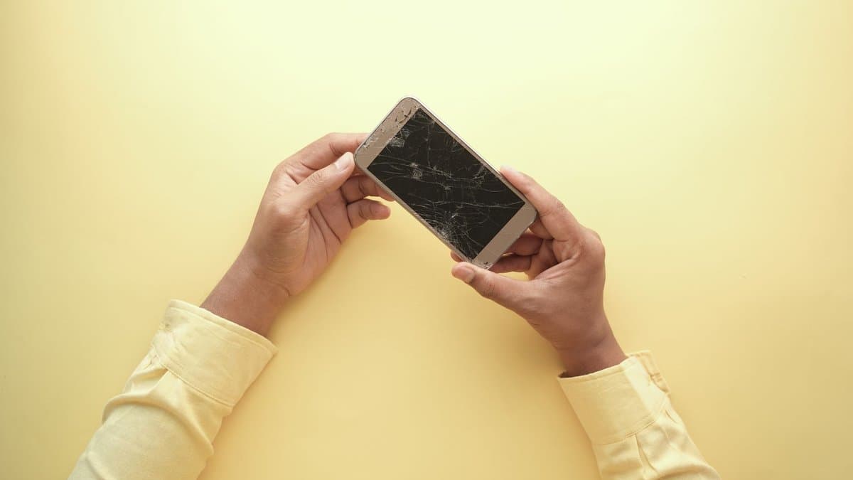 Zwei Hände halten ein Smartphone, dessen Display quer über die ganze Fläche gesprungen ist