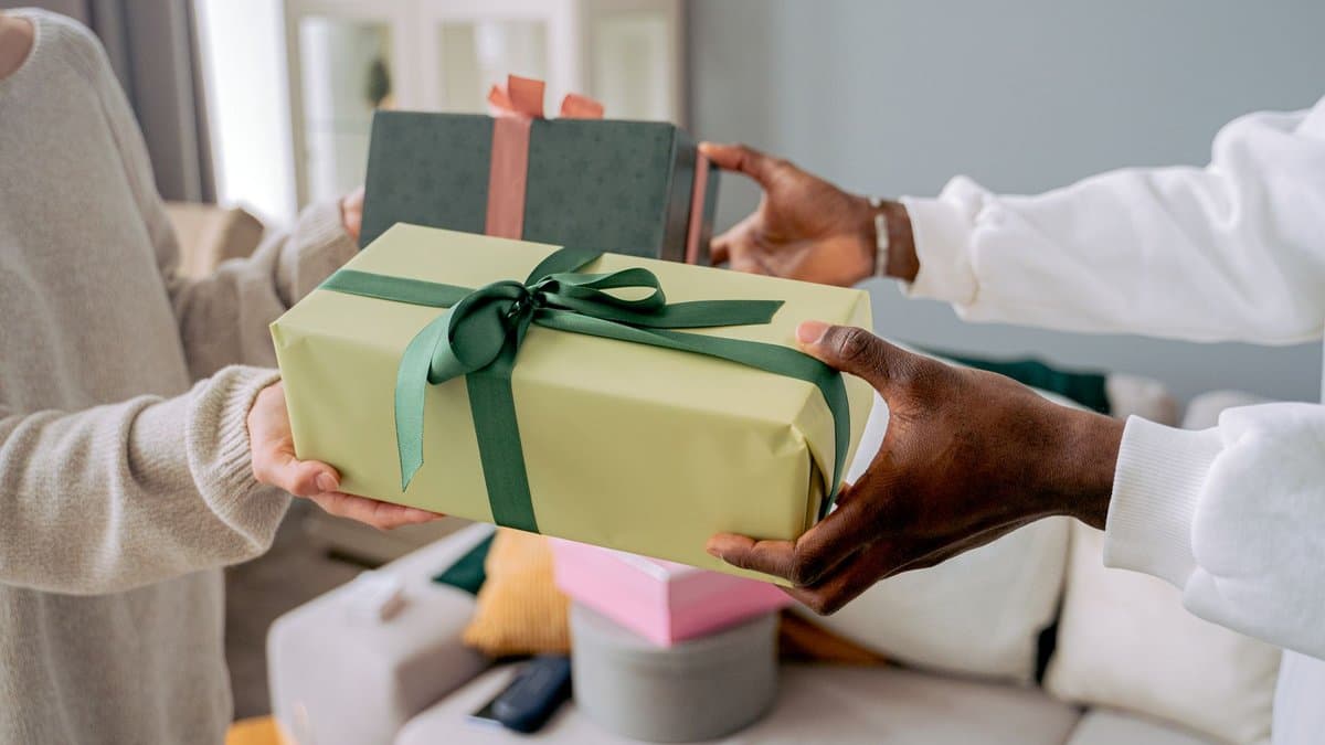 Zwei Personen reichen einander ein in grünes Papier eingeschlagenes Geschenk mit dunkelgrüner Schleife