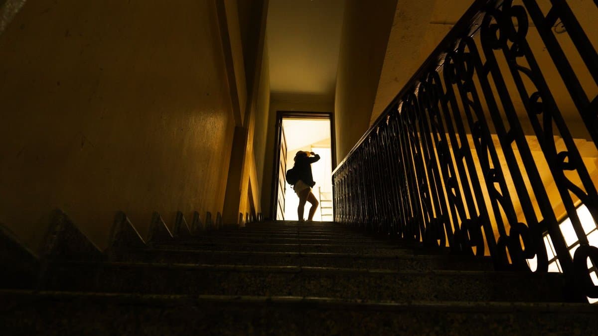 Silhouette einer Person in einem dunklen Treppenhaus, die auf eine hell erleuchtete Tür zugeht