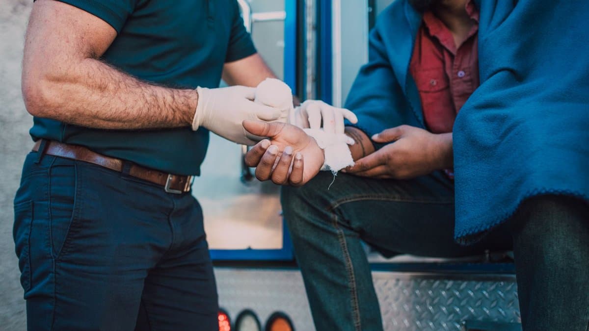 Sanitäter versorgt am Rettungswagen die verletzte Hand eines Mannes, der in eine Decke gehüllt auf der Ladekante sitzt