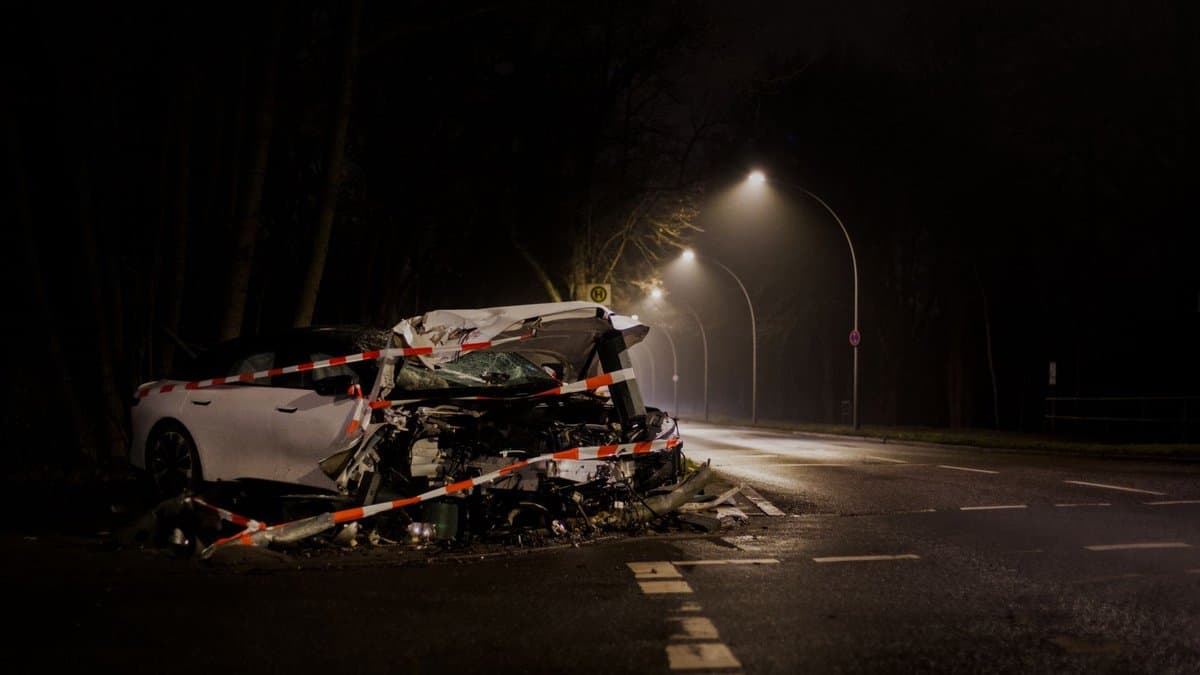 Nachts an einem Baum stehendes Unfallauto mit zerstörter Front, mit rot-weißem Absperrband gesichert