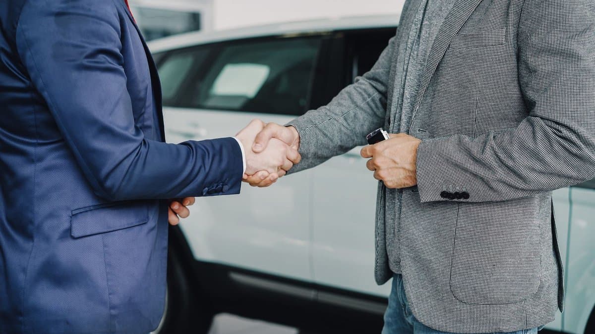 Zwei Männer geben sich vor einem Auto die Hand, einer hält einen Autoschlüssel in der Hand