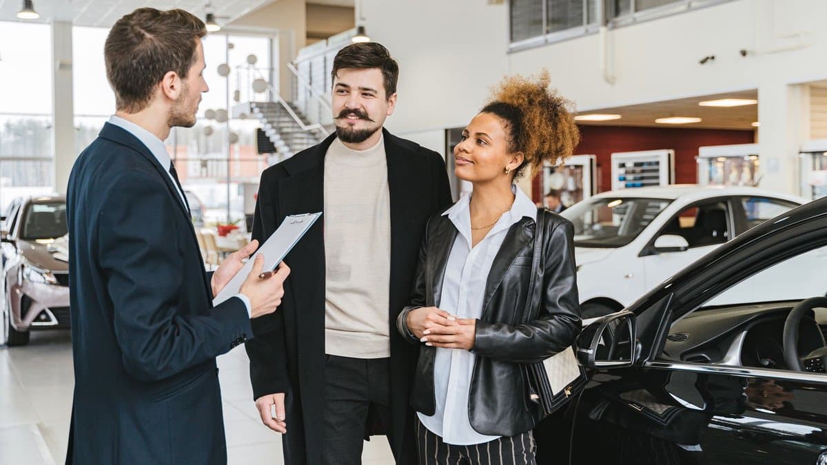 Ein Autoverkäufer mit Klemmbrett berät ein Paar im Ausstellungsraum eines Autohauses