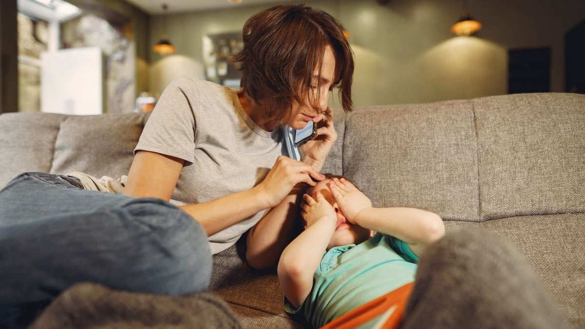 Mutter telefoniert auf dem Sofa und tröstet dabei ihr krankes Kind