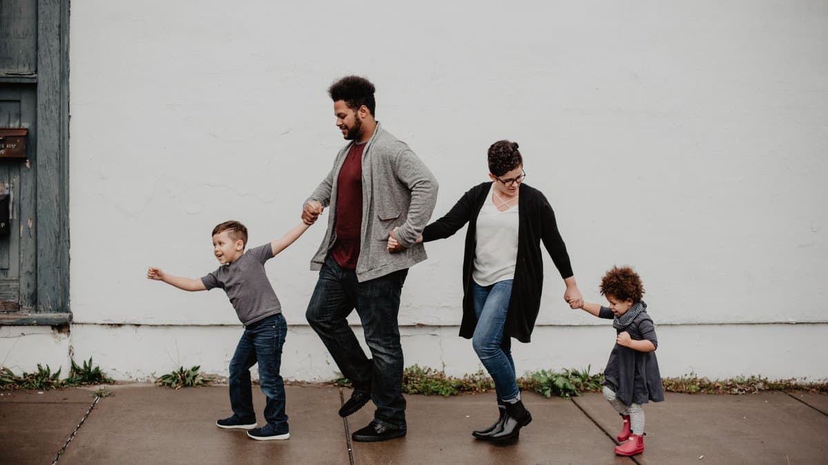Eltern gehen mit ihren beiden Kindern an den Händen einen Gehweg entlang